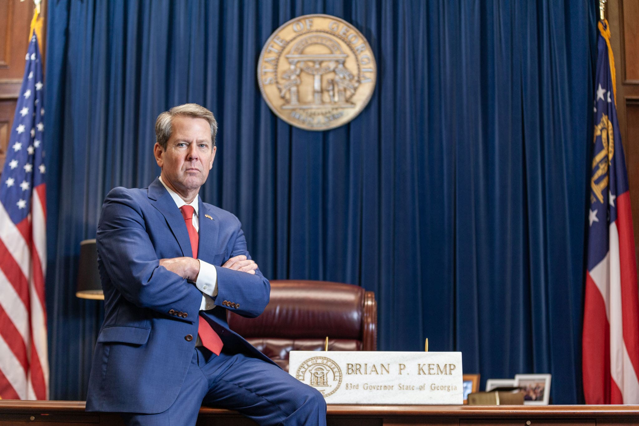 Georgia Governor Brian Kemp sitting with arms folded on his desk at the Georgia State Capitol.