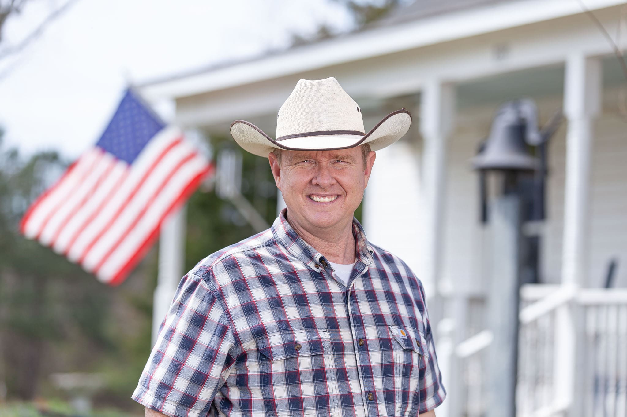 Georgia-State-Representative-and-helicopter-pilot-David-Jenkins-wearing-a-cowboy-hat-standing-in-front-of-his-farmhouse-with-an-American-flag-in-the-background.