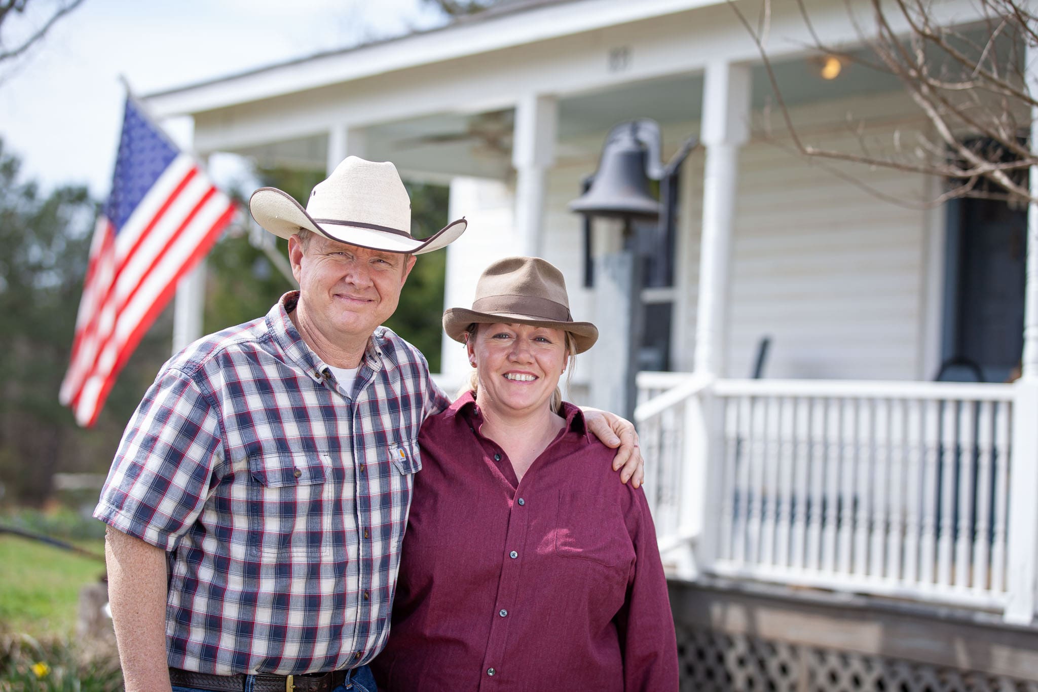 Georgia-State-Representative-and-helicopter-pilot-David-Jenkins-and-his-wife-Cat-standing-in-front-of-their-farmhouse-with-an-American-flag-in-the-background