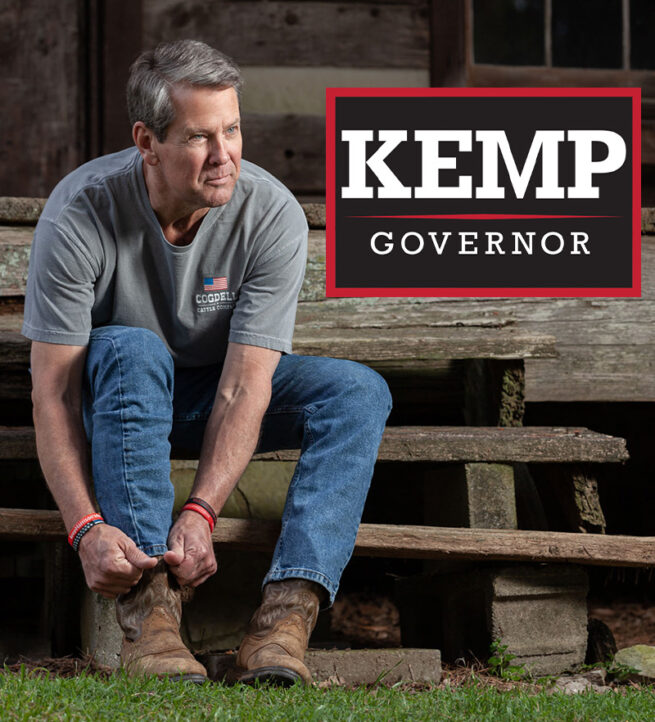 georgia-governor-brian-kemp-putting-on-his-boots-on-cabin-step-with-campaign-logo-in-top-right-of-picture.
