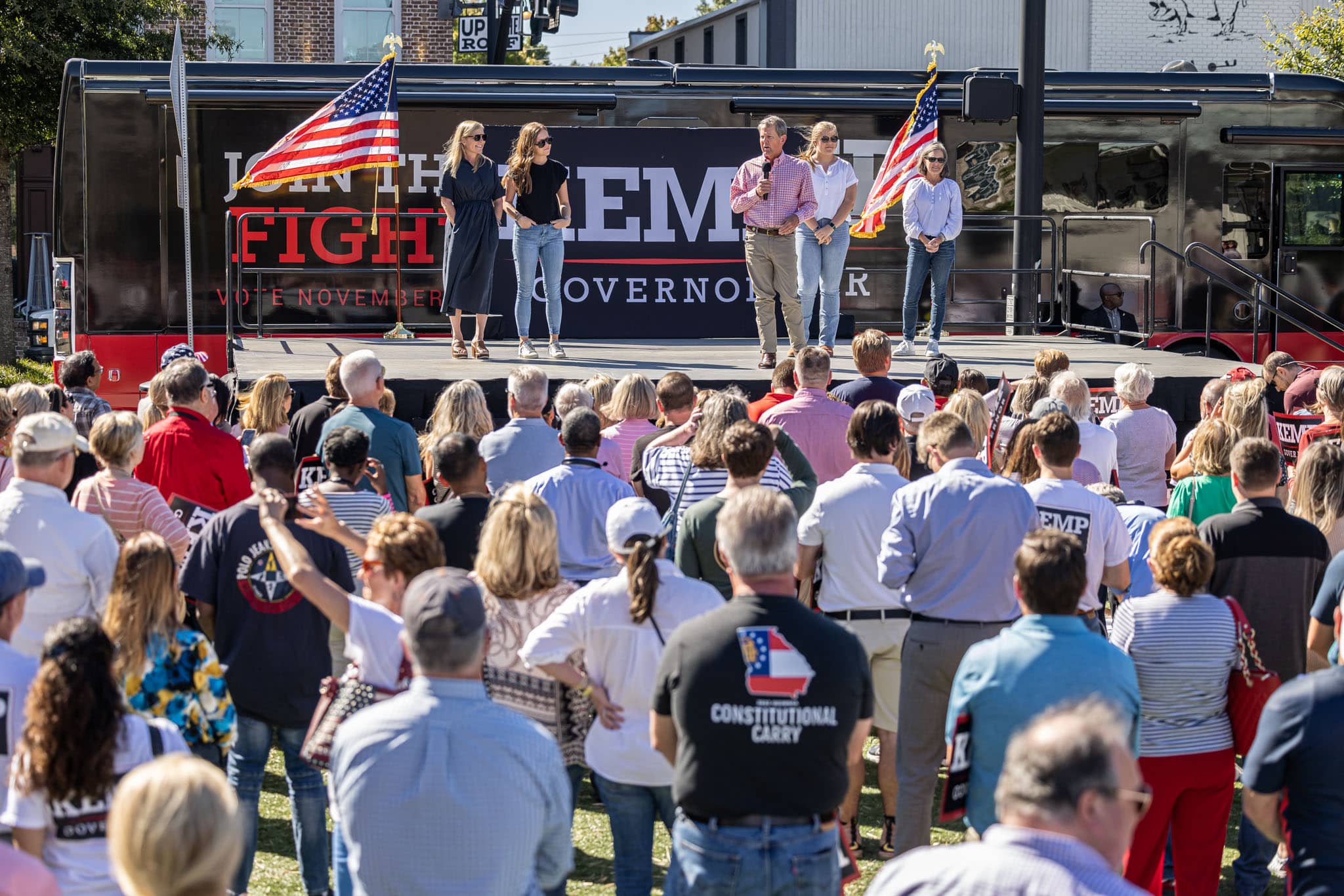 georgia-governor-kemp-speaking-on-stage-to-crowd-of-people-while-family-stands-behind-and-watch