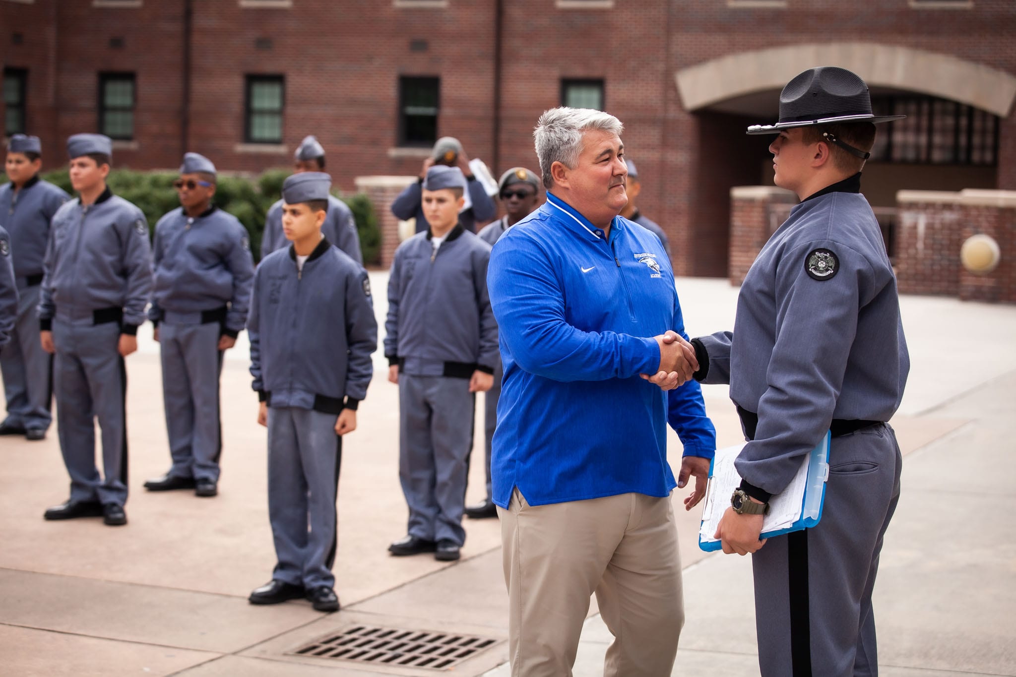 Lauren McDonald shaking hands with his son at, a cadet, at the Riverside Military Academy with other cadets in formation in the background.